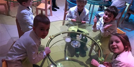 Powiększ grafikę: Uczniowie wokół szklanego stołu, oczekują na wyniki eksperymentu.