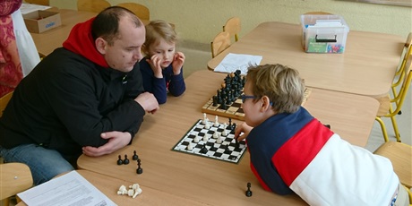 Powiększ grafikę: Rodzice z uczniami rozgrywają partię szachów.