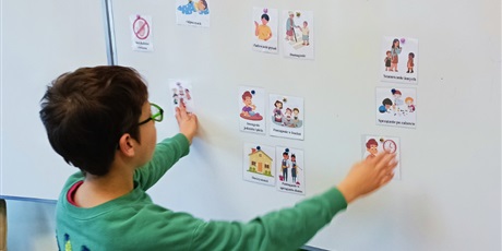 Powiększ grafikę: Chłopiec stoi twarzą do tablicy i segreguje ilustrację na prawą i obowiązki.