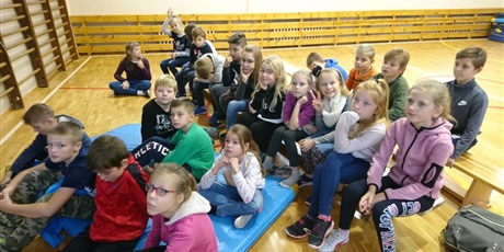 Powiększ grafikę: Uczniowie zgromadzeni na sali gimnastycznej przysłuchują się prowadzącej.