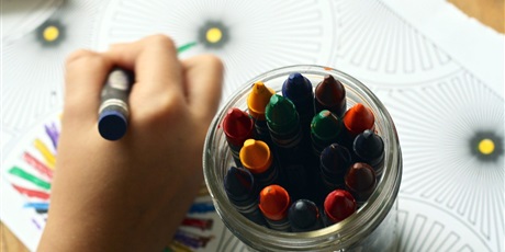 Powiększ grafikę: Grafika poglądowa - ręka dziecka rysująca obrazek; obok słoiczek z kredkami świecowymi.