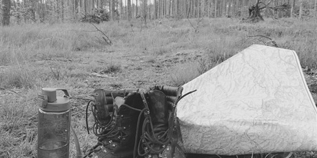 Powiększ grafikę: Środek lasu, na pierwszy planie buty wojskowe, butelka z wodą i ozdobny papier. 