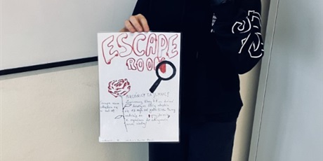 Powiększ grafikę: Na zdjęciu uczennica klasy 7B trzymająca plakat zapraszający do wzięcia udziału w Escape room.