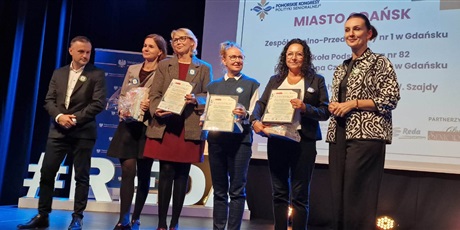Powiększ grafikę: Grupa osób na scenie z certyfikatami.