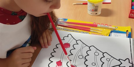 Powiększ grafikę:  Uczeń trzyma w ustach pędzel i koloruje obrazek choinki. 