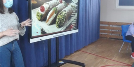 Powiększ grafikę: Wolontariuszka z Włoch przedstawia regionalne potrawy (prezentacja na ekranie multimedialnym).