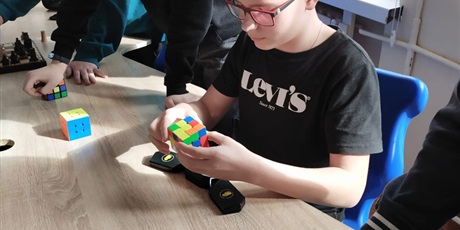 Powiększ grafikę: Uczeń układa kostkę Rubika.