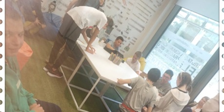 Powiększ grafikę: uczniowie siedzą wokół stołu i wykonują zadanie na kartkach.